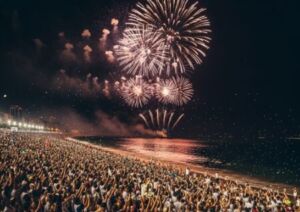 Multidão vestida de branco na praia de Copacabana assistindo a fogos de artifício no Réveillon no Brasil.