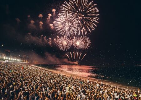 Multidão vestida de branco na praia de Copacabana assistindo a fogos de artifício no Réveillon no Brasil.